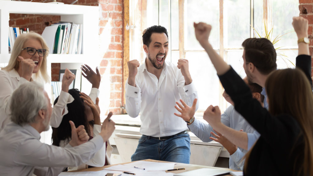 Euphoric excited business team celebrate corporate victory together in office